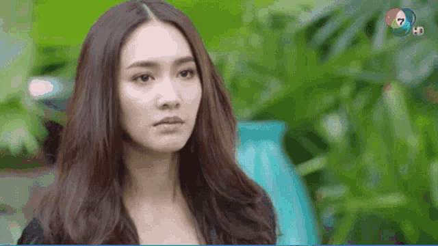 a woman with long brown hair is standing in front of a blue vase and looking at the camera .