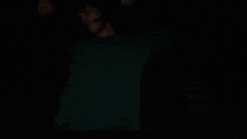 a person in a green shirt is standing in the dark with their hands up in the air .