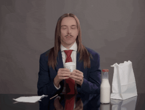 a man with long hair and a mustache is sitting at a table with a bottle of milk and a paper bag