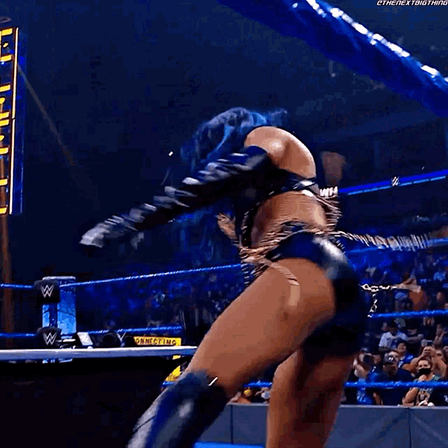 a woman with blue hair is dancing in a wrestling ring while a crowd watches .