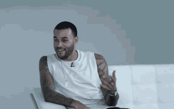 a man with tattoos on his arms is sitting on a couch with his arm outstretched