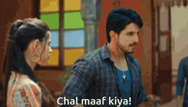 a man and a woman are standing in front of a window and the man is saying " chal maaf kiya "