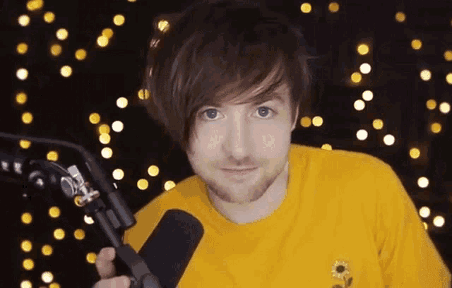 a young man in a yellow shirt is holding a microphone