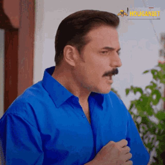 a man with a mustache wearing a blue shirt with the word holidaybet in the corner