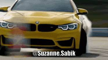 a yellow bmw is drifting on a track with the name suzanne.sabik on the bottom right