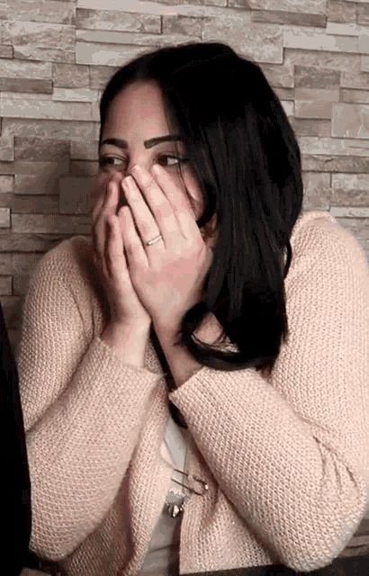 a woman in a pink sweater covering her face with her hands