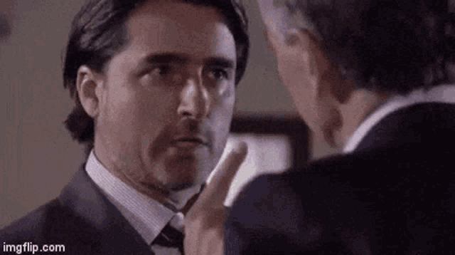 two men in suits and ties are talking to each other in a room .