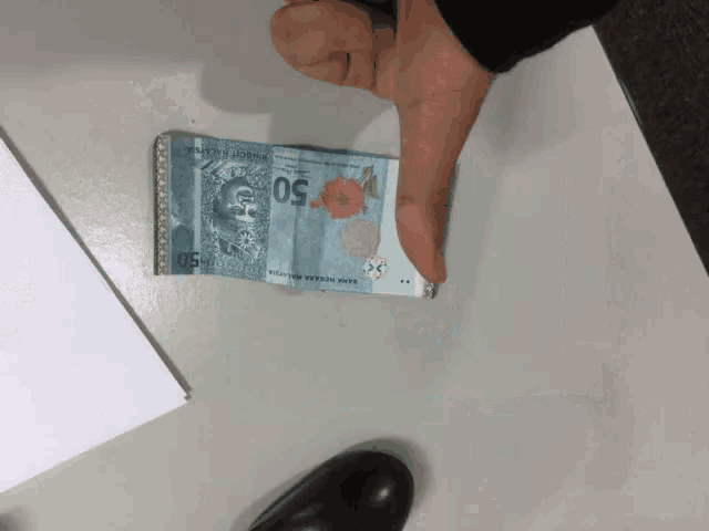a person is pointing at a 50 malaysian currency bill