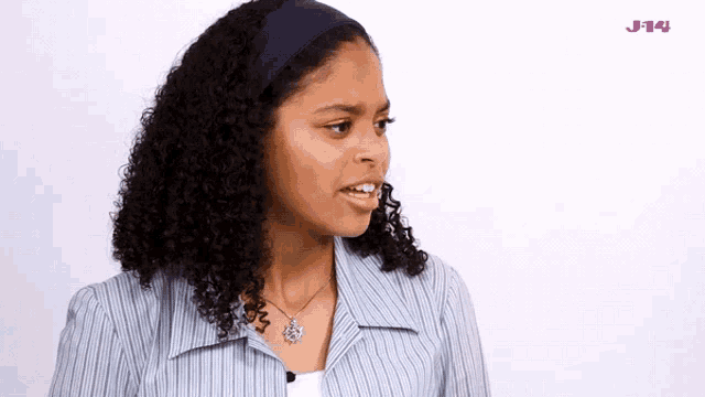a woman with curly hair and a necklace with a j14 logo in the corner