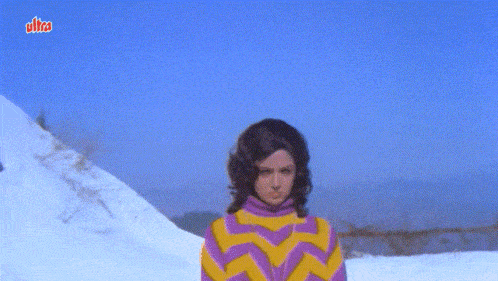 a woman in a yellow and purple striped sweater is standing in the snow in front of a blue sky with ultra written on it