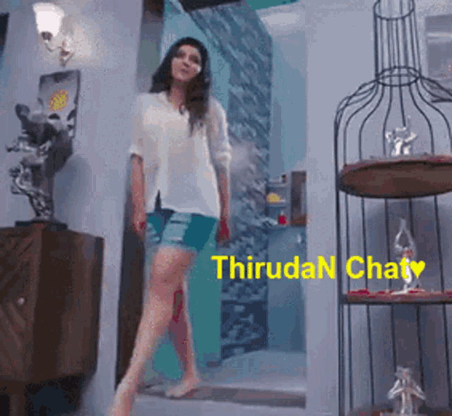 a woman in a white shirt and blue shorts is walking in a room with the words " thiruda chat " on the bottom right