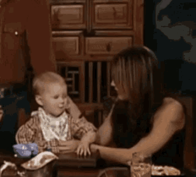 a woman and a baby are sitting at a table . the baby is wearing a bib .