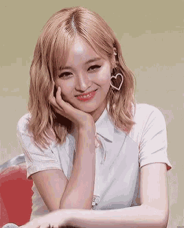 a young woman with blonde hair and heart shaped earrings is smiling with her hand on her chin .