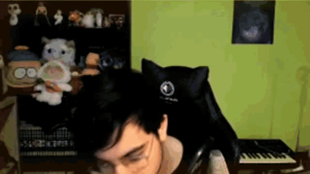 a man is sitting in a chair with a cat on his head in front of a keyboard .