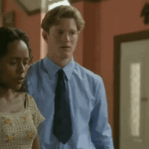 a man and woman are standing next to each other in a room . the man is wearing a blue shirt and tie .