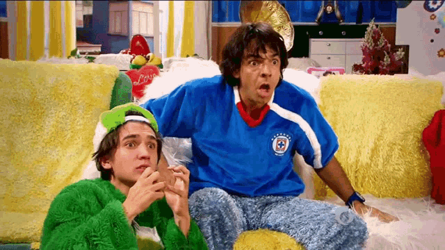 two men are sitting on a couch one is wearing a blue shirt with the word cruz on it