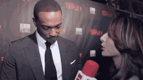 a man in a suit and tie is being interviewed by a woman in front of a microphone .