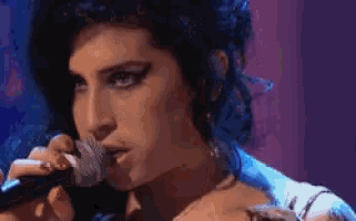 a woman is singing into a microphone with a cigarette in her mouth .