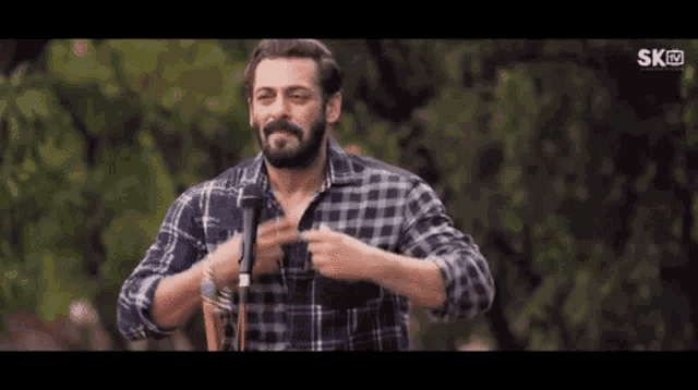 a man with a beard wearing a plaid shirt is holding a microphone .