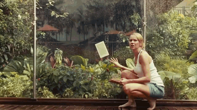 a woman is squatting down in front of a window holding a piece of paper in her hand