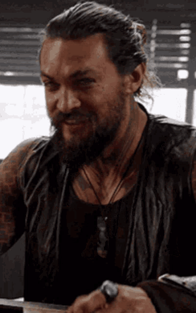 a man with a beard is wearing a black leather vest and a ring on his finger