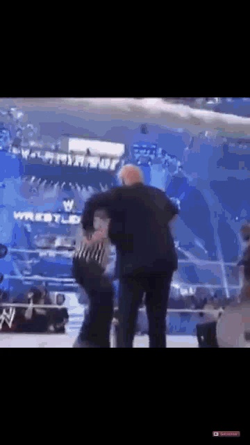 a man in a suit is standing in a wrestling ring holding a referee 's hand .