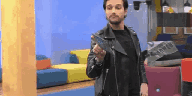 a man in a leather jacket is standing in a living room holding a wallet .