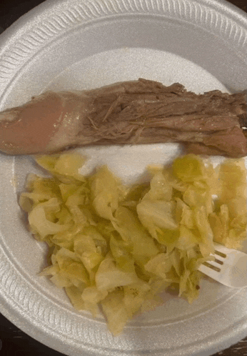 a styrofoam plate with a piece of meat and a side of cabbage