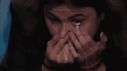 a man is crying while covering his face with his hands and a tear is coming out of his eye .