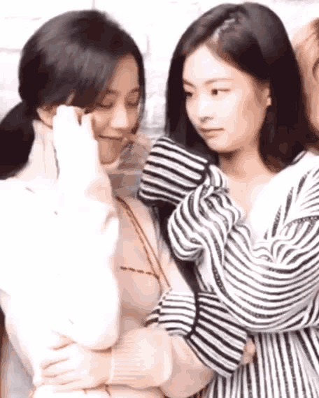 two women are standing next to each other and hugging each other . one of the women is wearing a striped shirt .