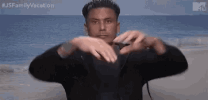 a man is making a heart with his hands on the beach .