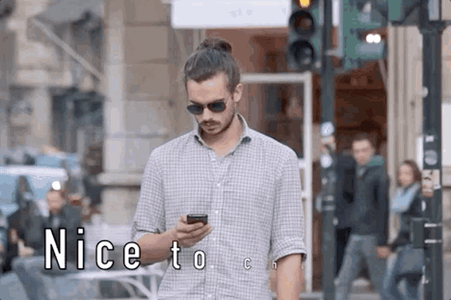 a man is walking down a street while looking at his cell phone .