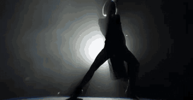 a silhouette of a woman in a black dress is dancing in the dark