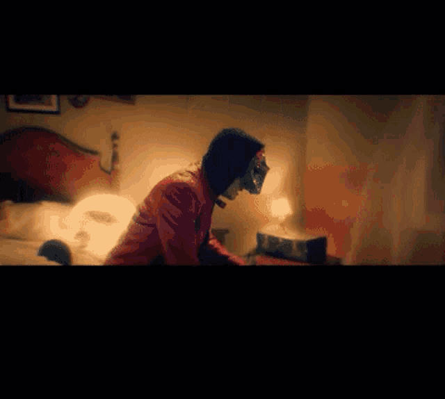 a man wearing a mask and a red jacket is sitting on a bed