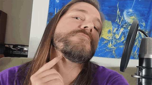 a man with long hair and a beard is pointing at his beard