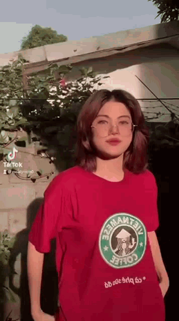 a woman in a red starbucks t-shirt is standing in front of a building .