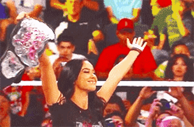 a woman is holding up a trophy in front of a crowd in a wrestling ring