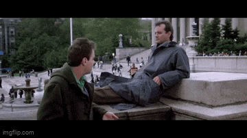 two men are sitting on a ledge talking to each other in a park .