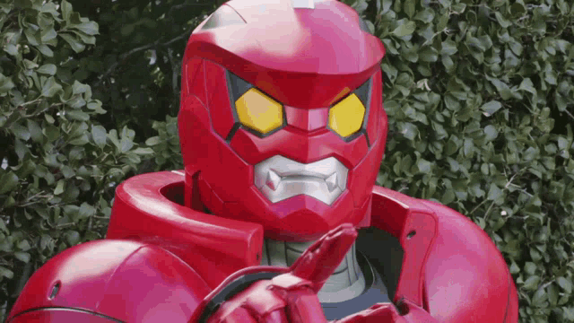 a red robot with yellow eyes is standing in front of trees