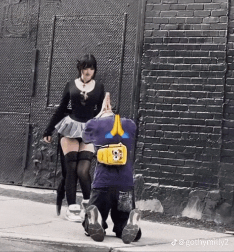 a woman in a skirt is standing next to a man with a yellow bag on his back .