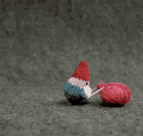 a knitted gnome is holding a knitted heart above a ball of yarn with the words feliz janeiro written below it