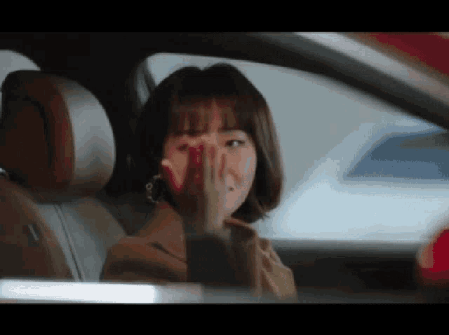 a woman is sitting in a car with her hand on her face .