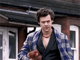 a man in a plaid robe is holding a chicken in front of a building .