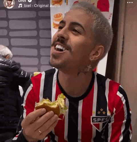 a man wearing a striped shirt is eating a hamburger .