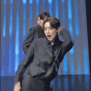 a man in a black shirt is dancing on a stage in front of a blue light .