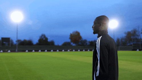a man in a black adidas jacket stands on a field
