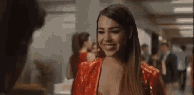 a woman in a red dress is smiling while standing next to a man in a hallway .