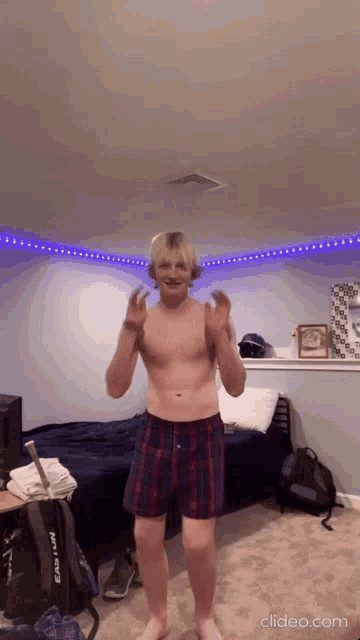 a shirtless man in plaid boxers is dancing in a bedroom with a backpack that says easton on it