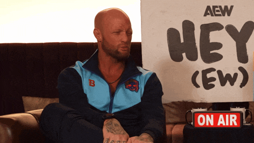 a man sits in front of a sign that says hey crew