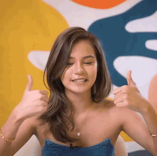 a woman giving two thumbs up in front of a colorful wall